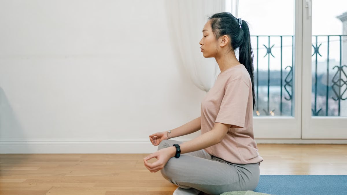 Asian woman meditating indoors on a yoga mat, exuding calm and serenity.