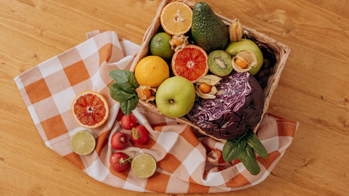 A colorful mix of fruits and vegetables arranged in a basket on a rustic wooden table.